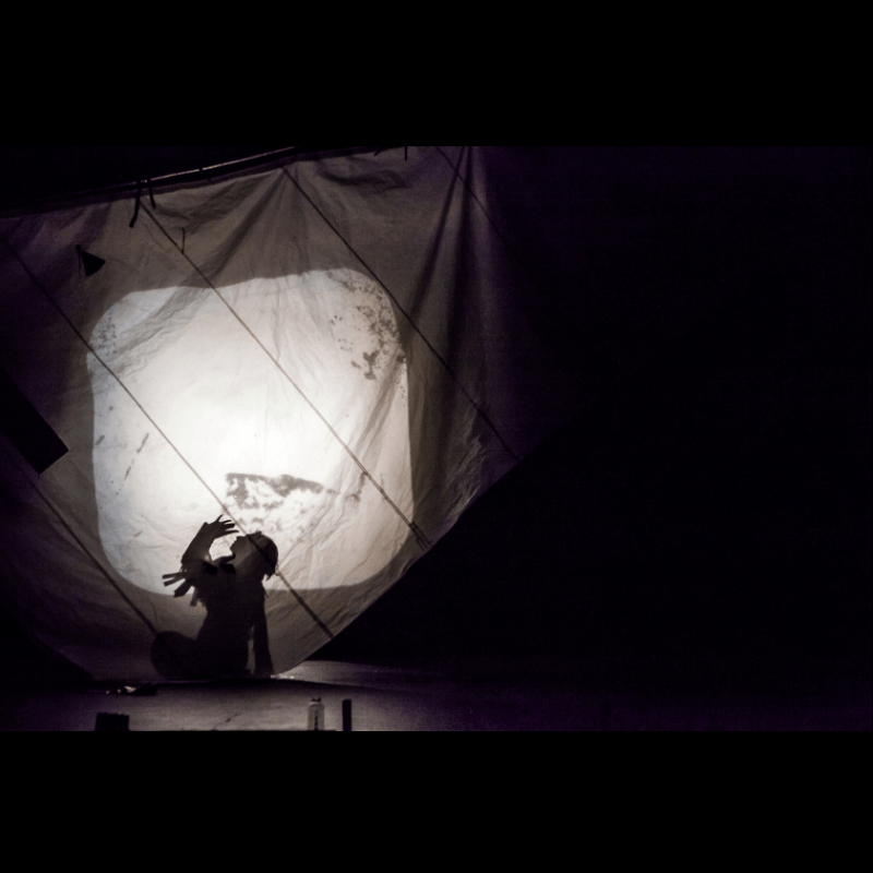 Image Description: A black and white photo of an artist sitting in front of a shadow puppetry screen.