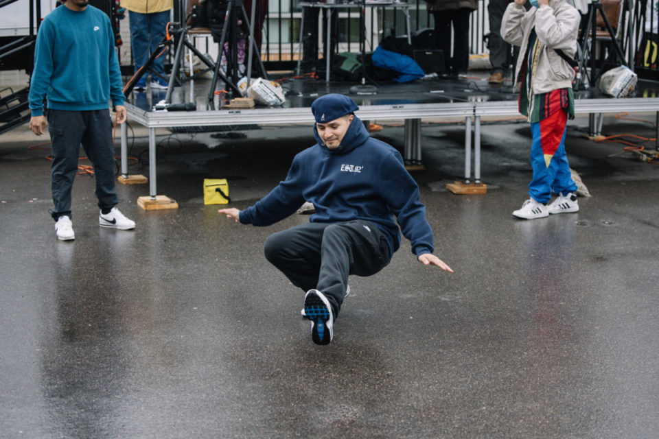 Image Description: a photo of one of the dancers from the Twin Citiez Breakerz kicks their foot out, low to the ground, mid-move.